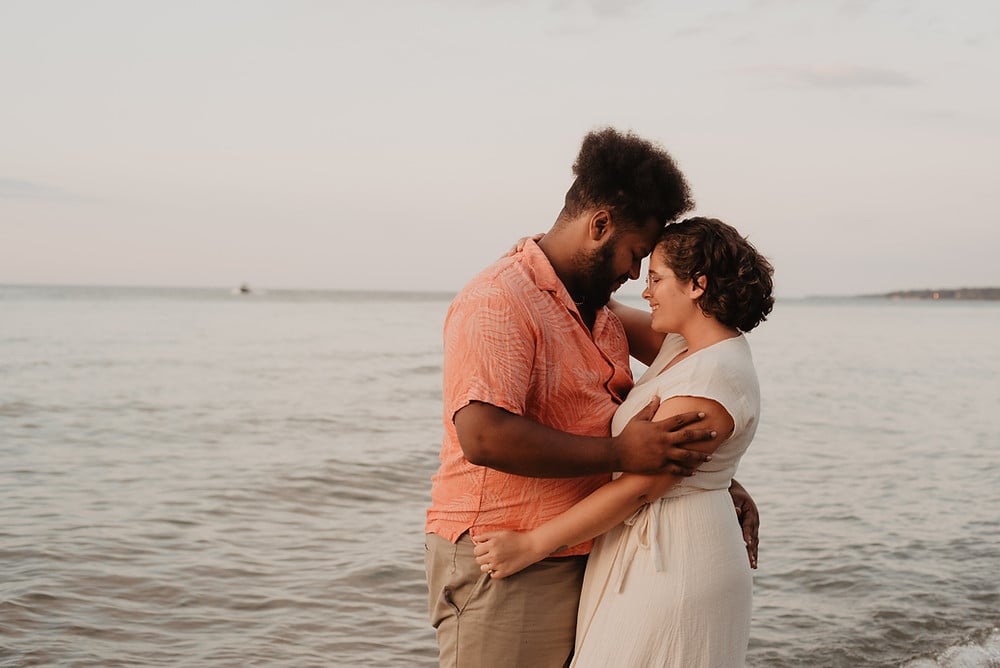 Couple standing by the water with their arms holding each other seemingly in love