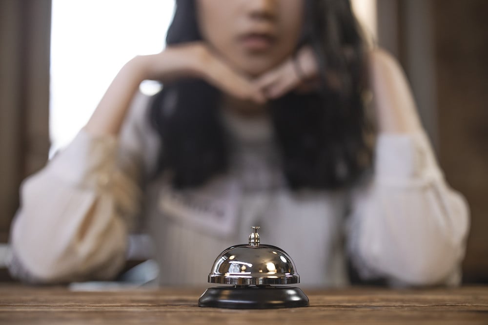 Woman sitting with hands under chin in front of bell she can ring if she needs help