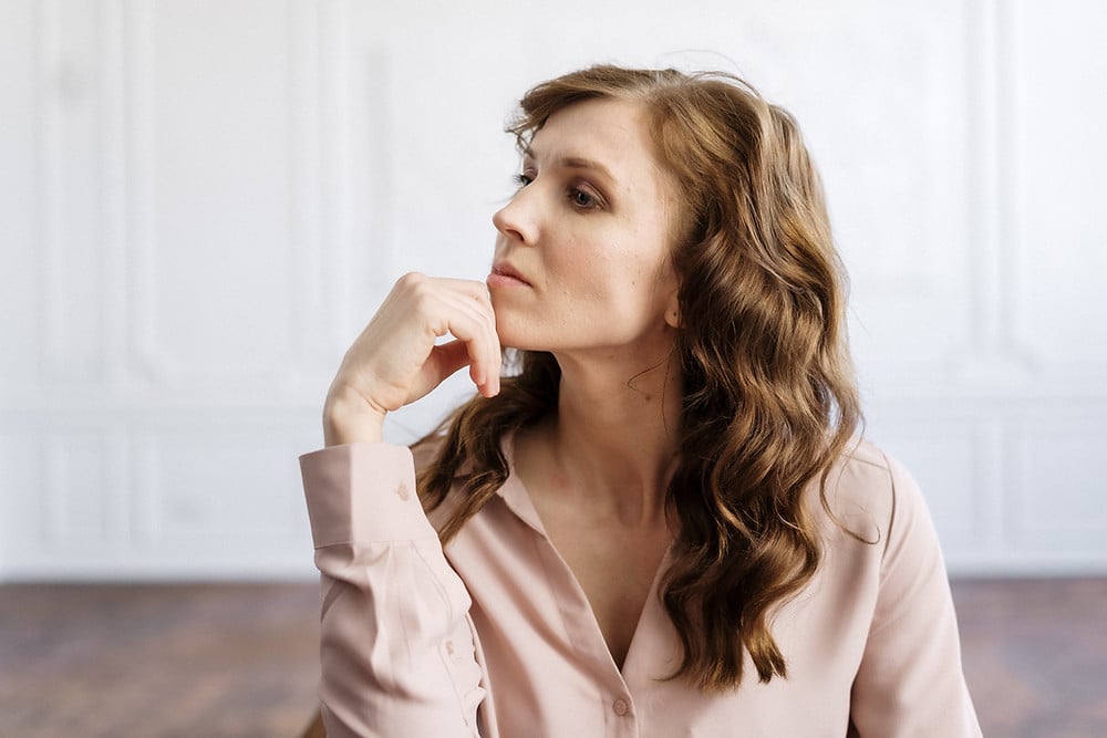 Woman sitting with hand on chin looking contemplative as she thinks about moving on after divorce