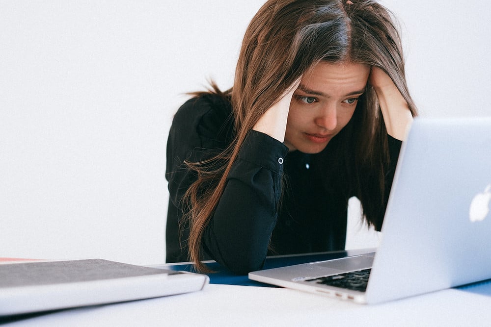 Woman sitting in front of laptop with hands in hair on side of head looking stressed