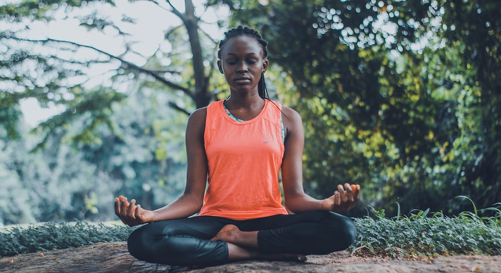 Woman sitting on ground around trees in meditation pose improving her spiritual health